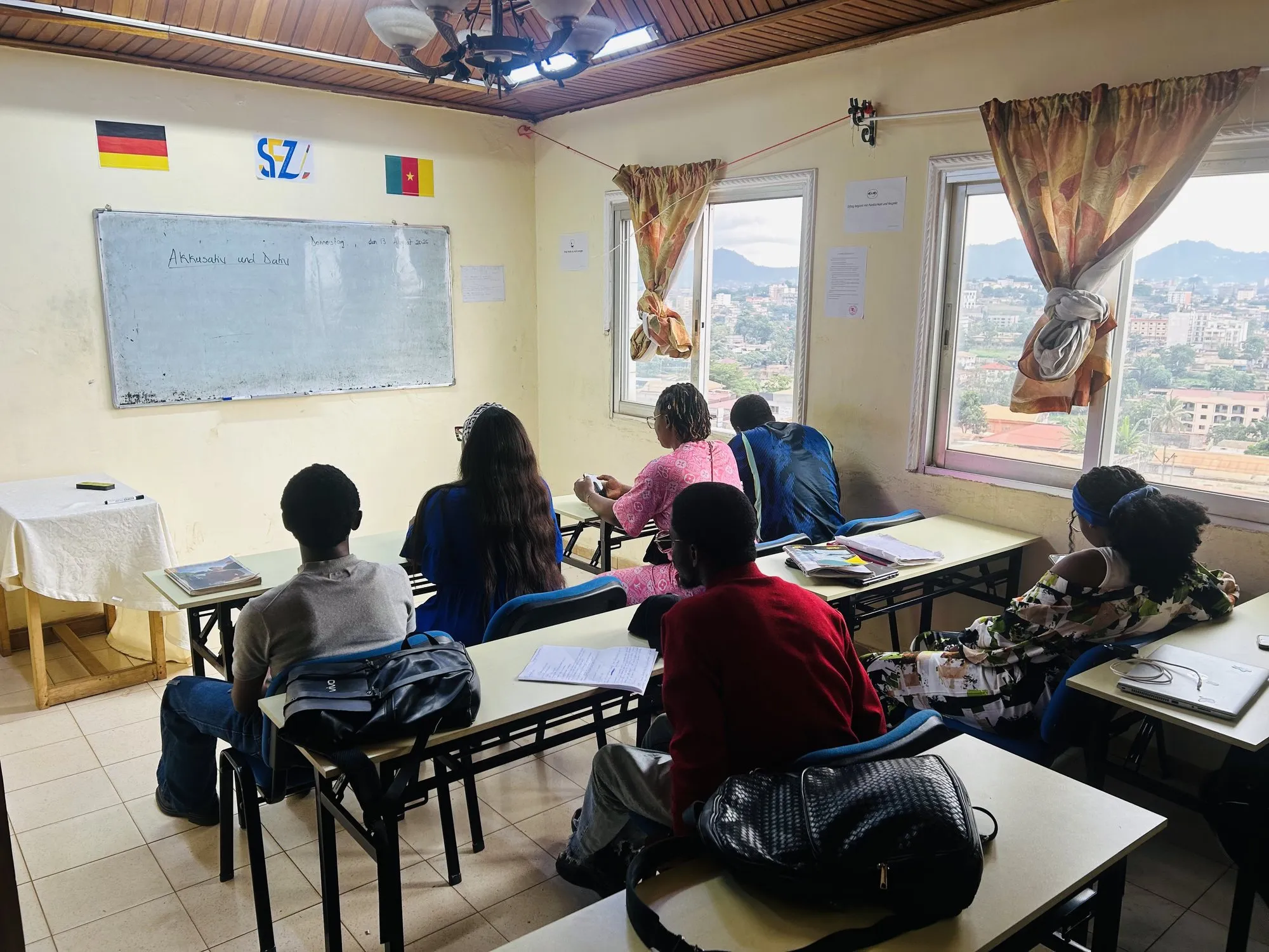 Salle de classe : des apprenants prennent des notes face au tableau marqué du logo SFZ