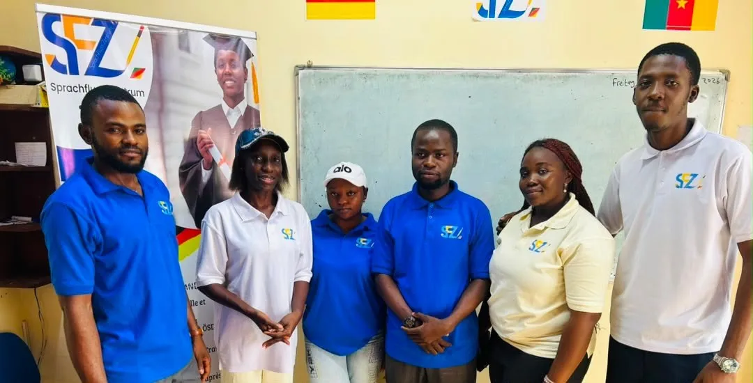 Six formateurs de Sprachfluss Zentrum Yaoundé en polos bleus et blancs devant le tableau de la salle de cours