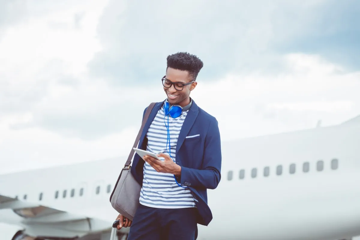 Ein junger Reisender schaut vor einem Flugzeug auf sein Tablet